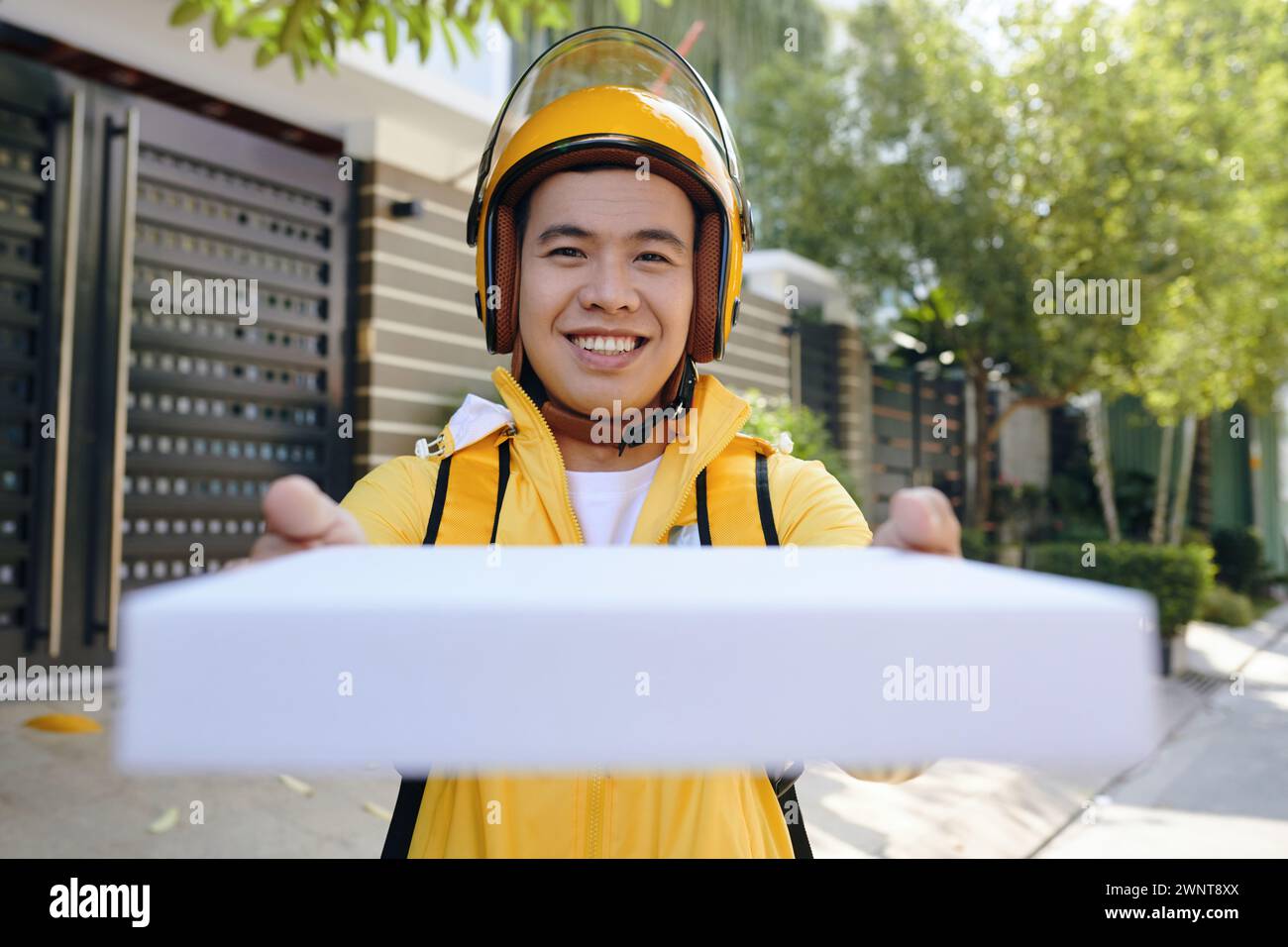 Livreur joyeux en uniforme jaune donnant boîte de pizza fraîche Banque D'Images