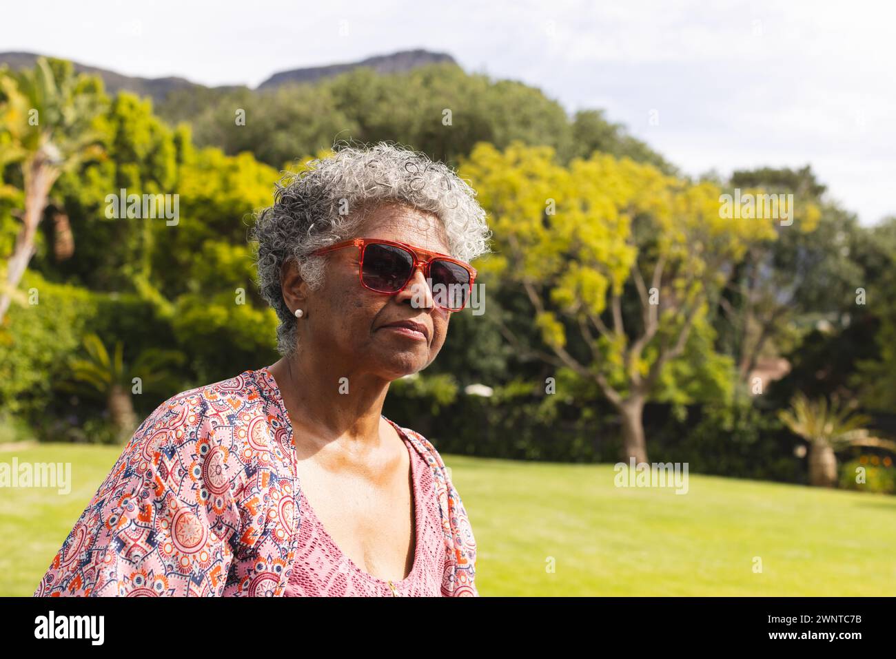 Femme biraciale senior avec les cheveux gris porte des lunettes de soleil rouges et une blouse à motifs, avec espace copie Banque D'Images