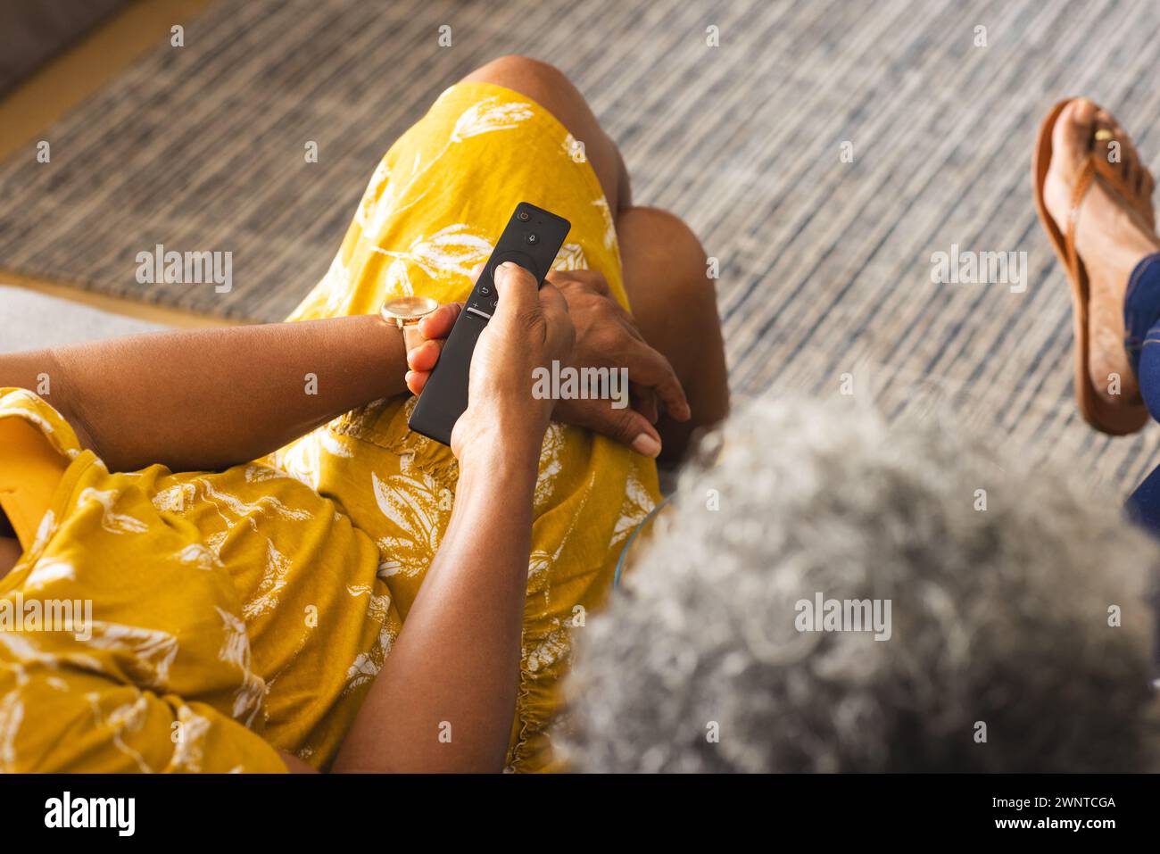 Senior afro-américaine dans une robe jaune tient un téléphone, assis à l'intérieur à la maison Banque D'Images