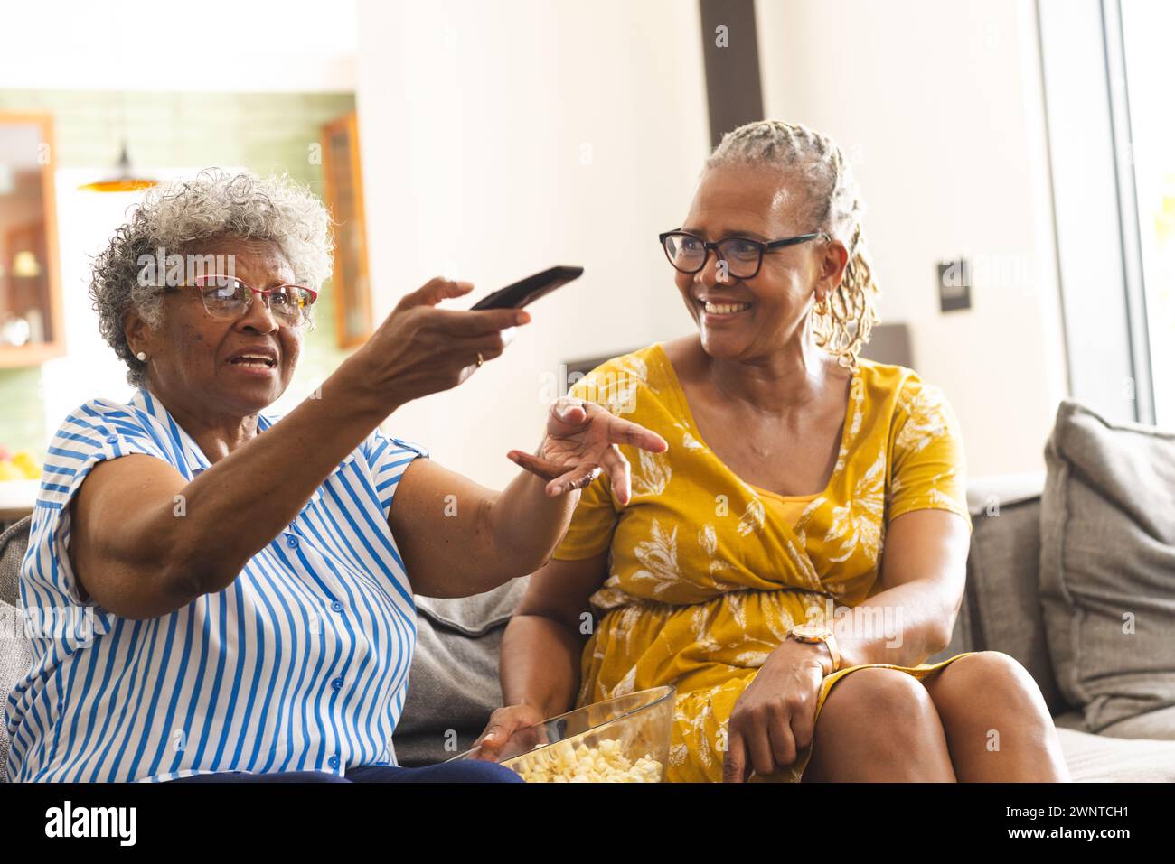 Une femme afro-américaine senior pointe vers la télévision avec une télécommande, tandis que son compagnon sourit à la maison Banque D'Images