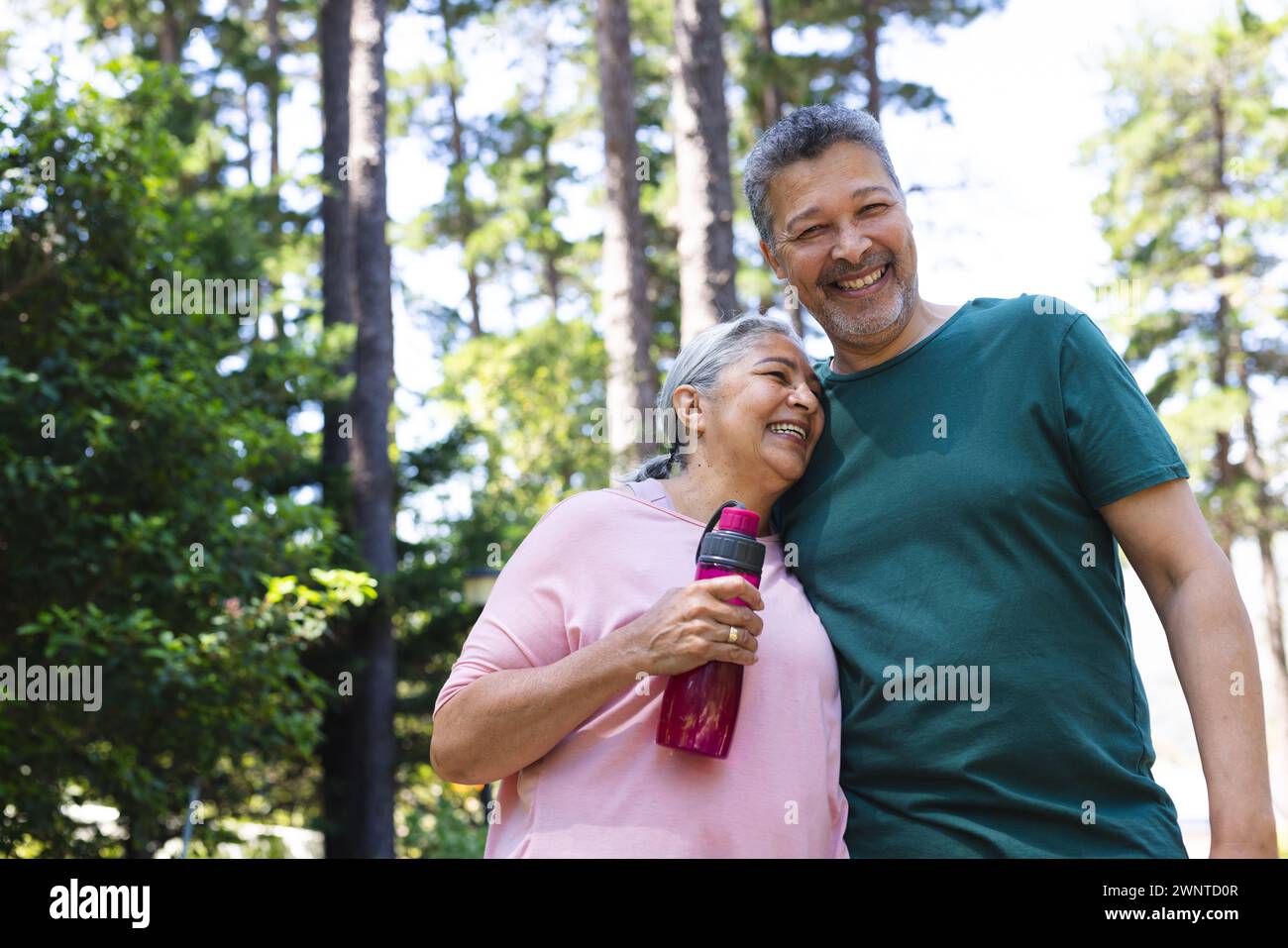 Couple biracial senior profite d'une journée ensoleillée à l'extérieur, avec la femme tenant une bouteille d'eau Banque D'Images