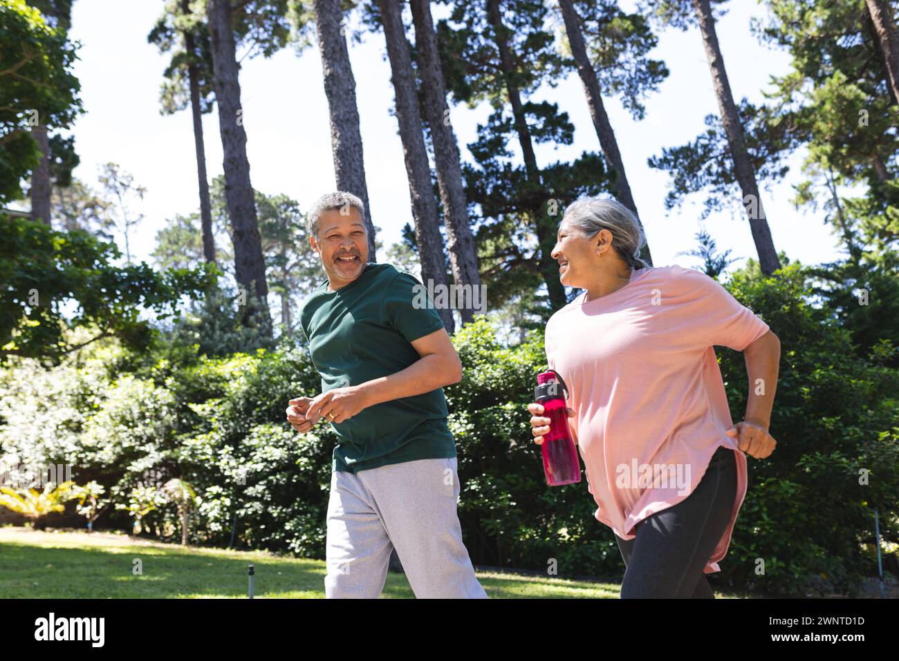 Couple biracial senior aime un jogging dans un parc ensoleillé Banque D'Images