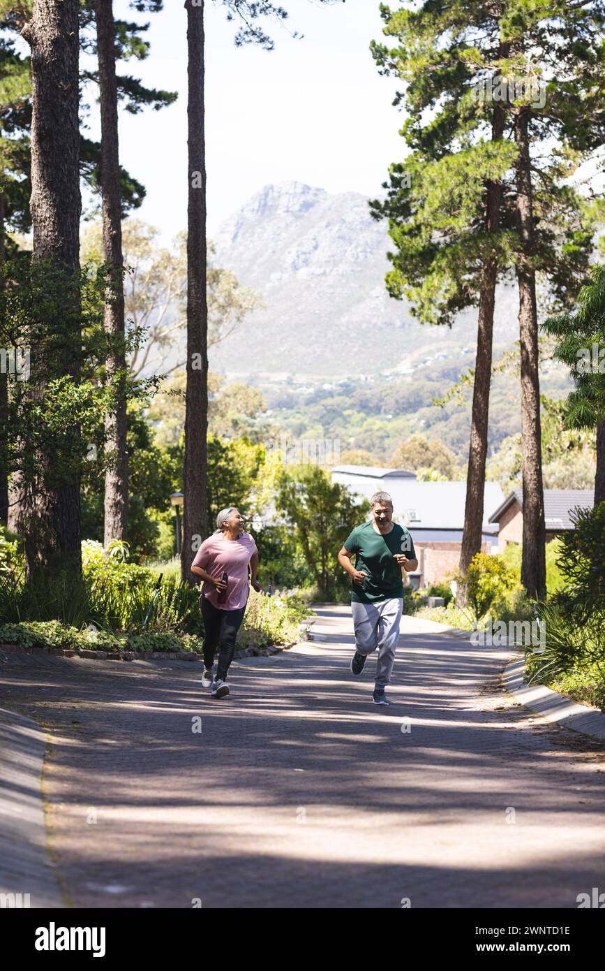 Femme biraciale senior et homme biracial jogging dans un chemin bordé d'arbres avec espace de copie Banque D'Images