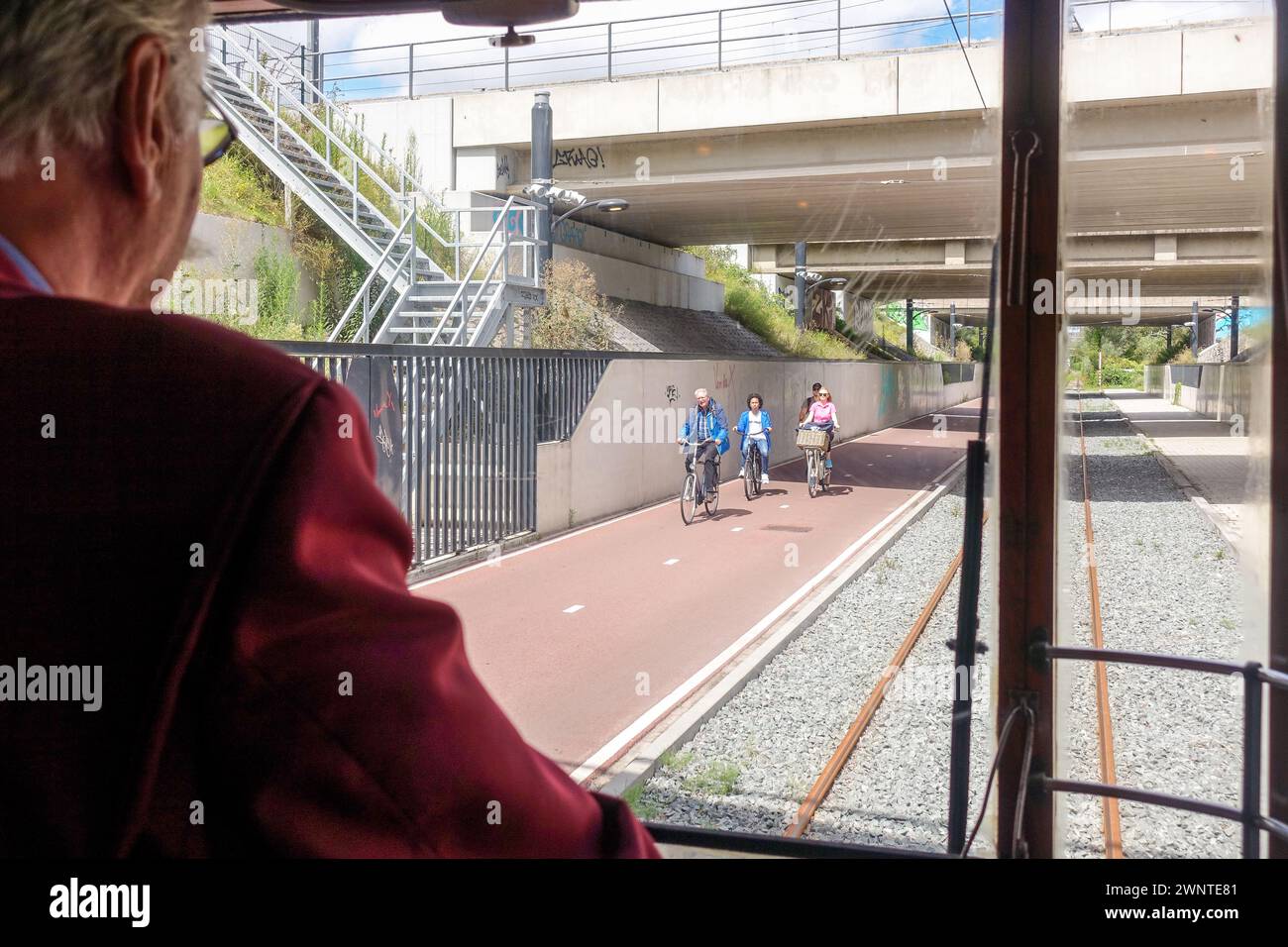 Vue depuis la fenêtre du tramway derrière le conducteur, des gens marchant et faisant du vélo sur un chemin de la ville sous un pont lors d'une journée ensoleillée à Amsterdam Banque D'Images