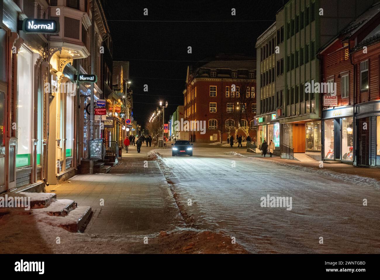 Scène de rue nocturne de la rue principale à Tromso, avec la rue couverte de neige et une voiture conduisant vers le bas avec des piétons sur les promenades latérales. Banque D'Images