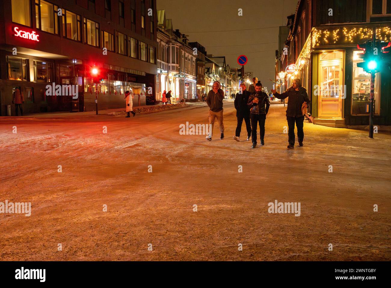 Groupe d'amis traverse la rue lors d'une nuit à Tromso, Norvège, dans le froid de l'hiver avec la rue couverte de neige et la promenade latérale Banque D'Images