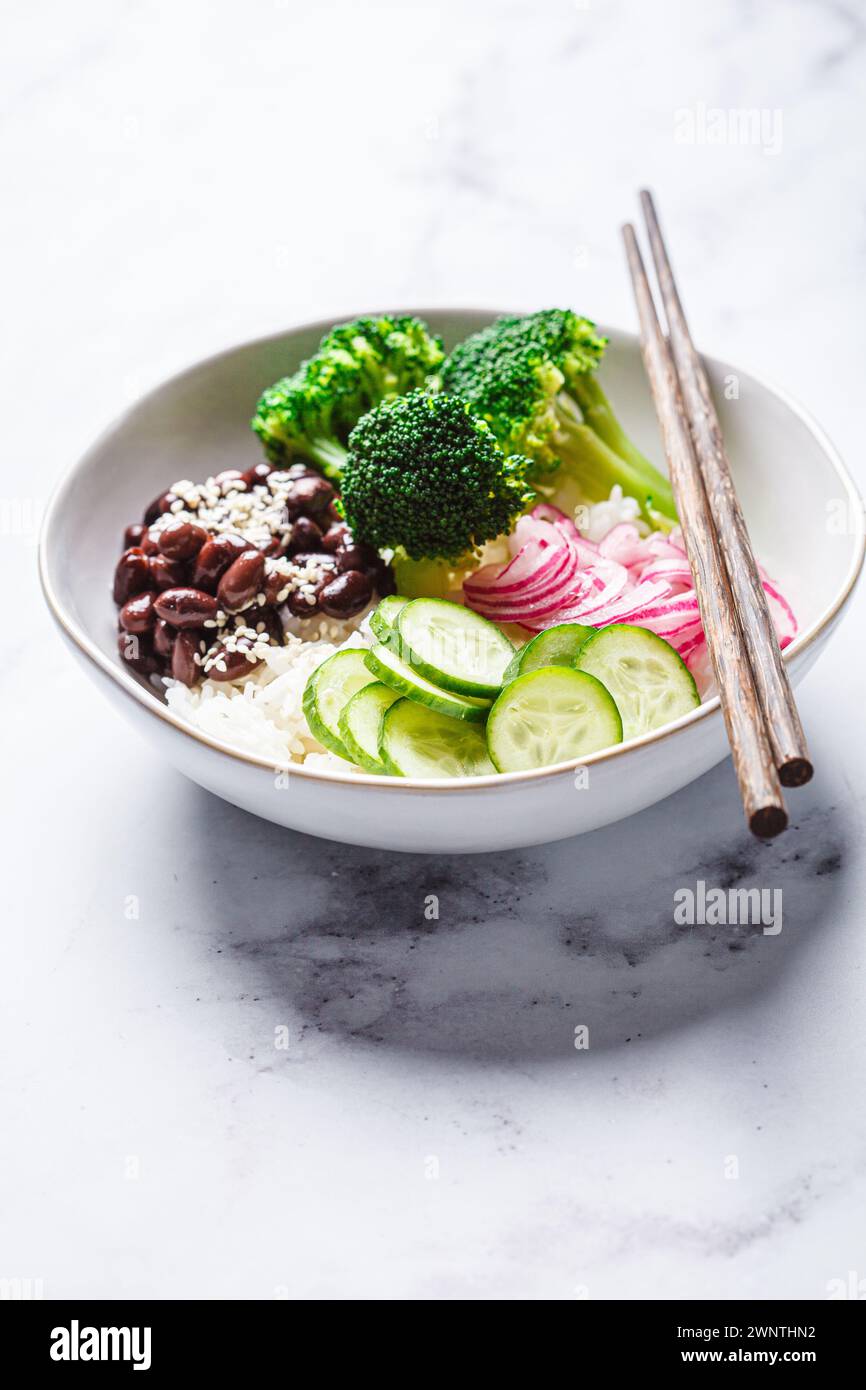 Bol vegan poke avec riz, brocoli, concombre, haricots et oignon rouge mariné, fond de marbre blanc. Banque D'Images