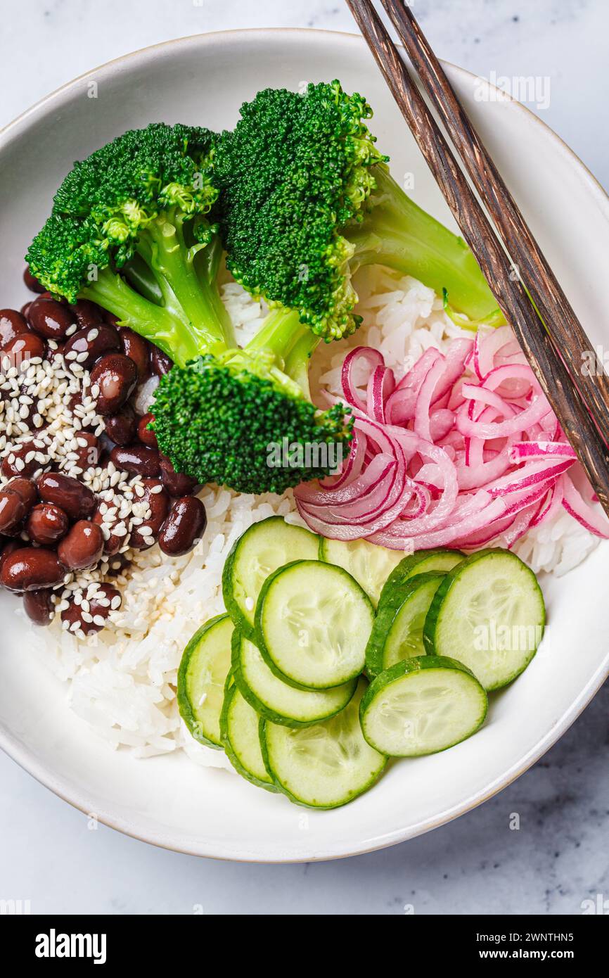 Vegan Poke. Bol avec riz, brocoli, concombre, haricots et oignon rouge mariné, fond de marbre blanc, vue de dessus. Banque D'Images