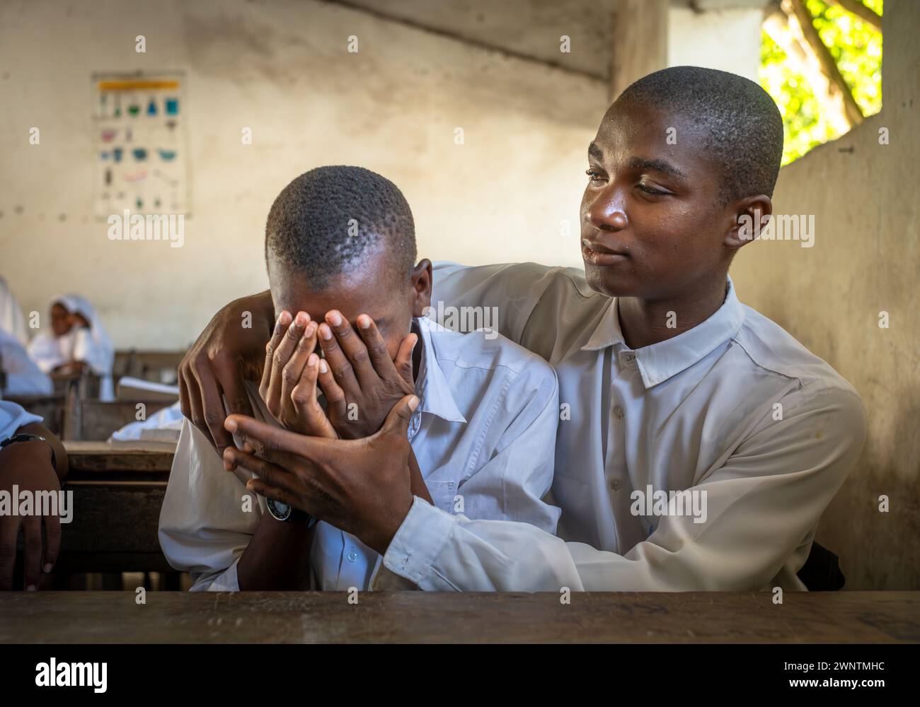 Un étudiant musulman réconforte son ami dans un cours d'anglais à l'école secondaire Jambiani à Jambiani, Zanzibar, Tanzanie. Banque D'Images