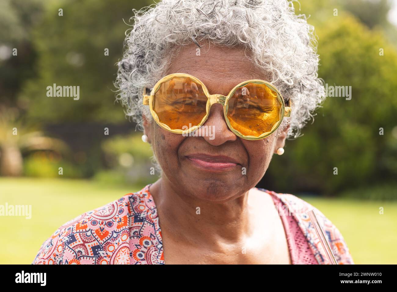 Femme biraciale senior avec les cheveux gris porte de grandes lunettes de soleil ambre et boucles d'oreilles en perles Banque D'Images