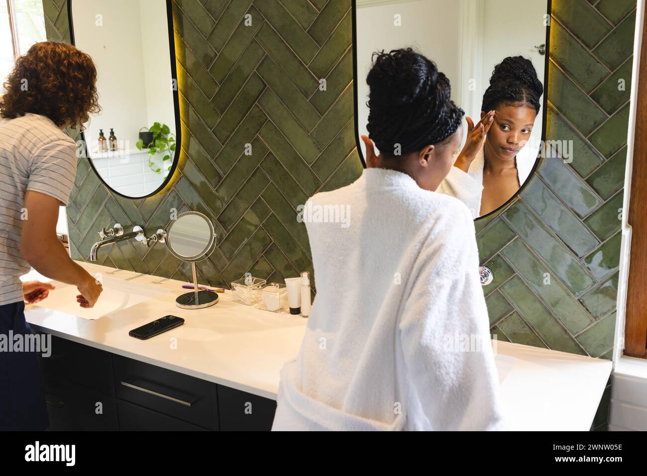 Couple diversifié : jeune femme afro-américaine applique le maquillage dans un miroir de salle de bain Banque D'Images