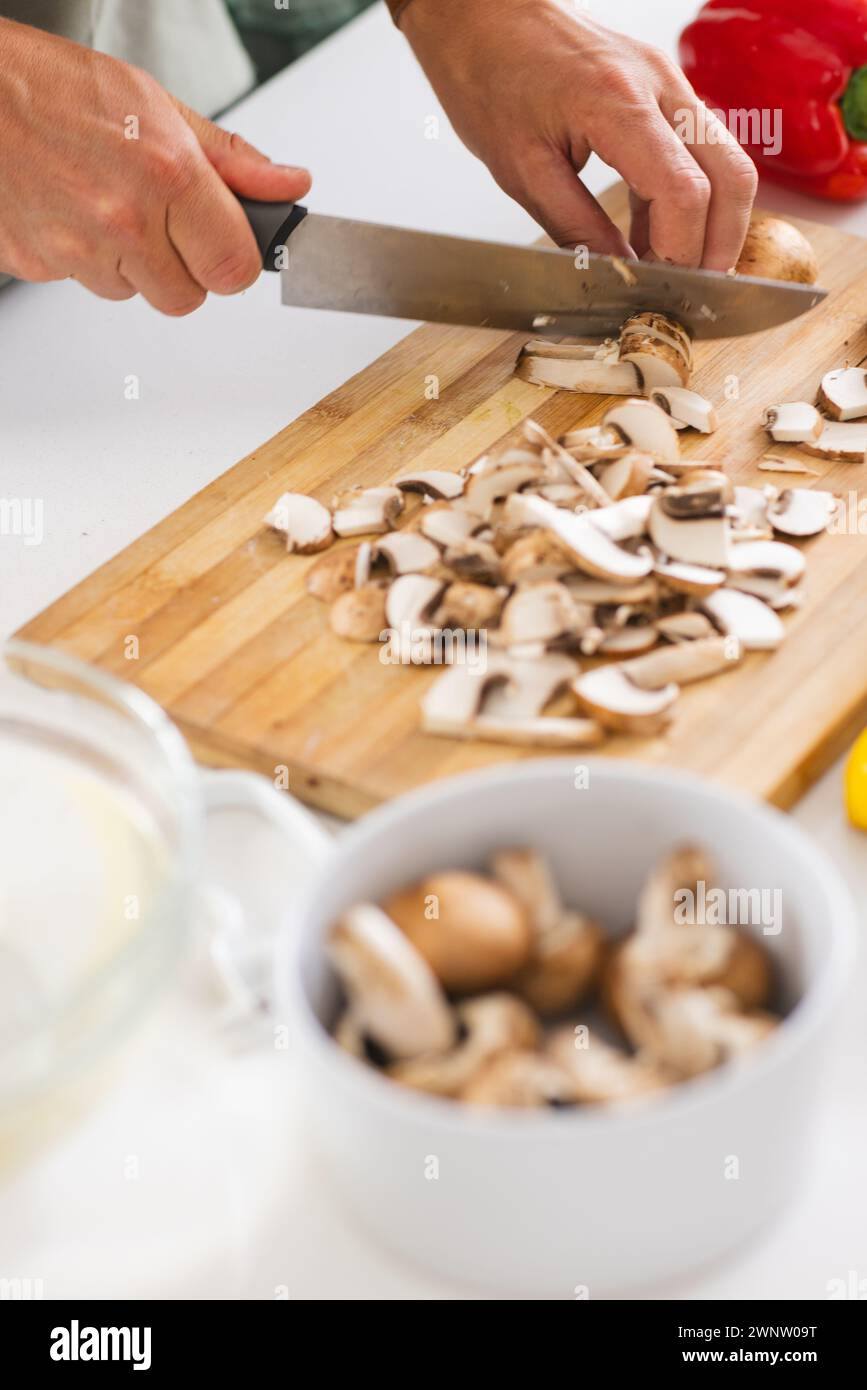 Les mains tranchent des champignons sur une planche à découper en bois avec un couteau de cuisine Banque D'Images