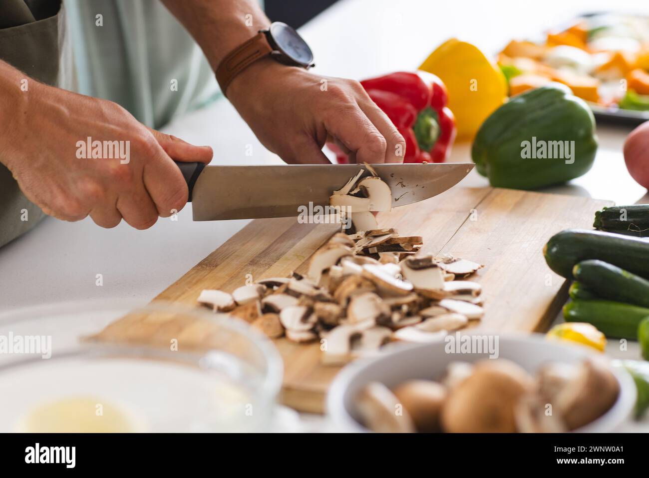 Une personne coupe des champignons sur une planche à découper blanche, entourée de poivrons colorés Banque D'Images