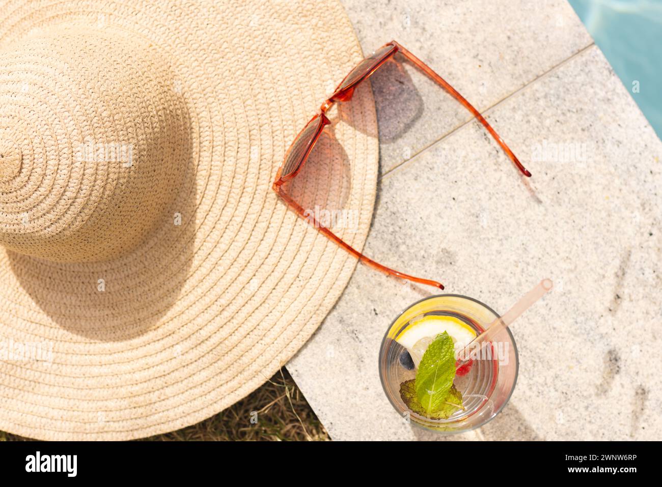 Un chapeau de paille, des lunettes de soleil et une boisson rafraîchissante sont assis sous la lumière du soleil avec un espace de copie Banque D'Images
