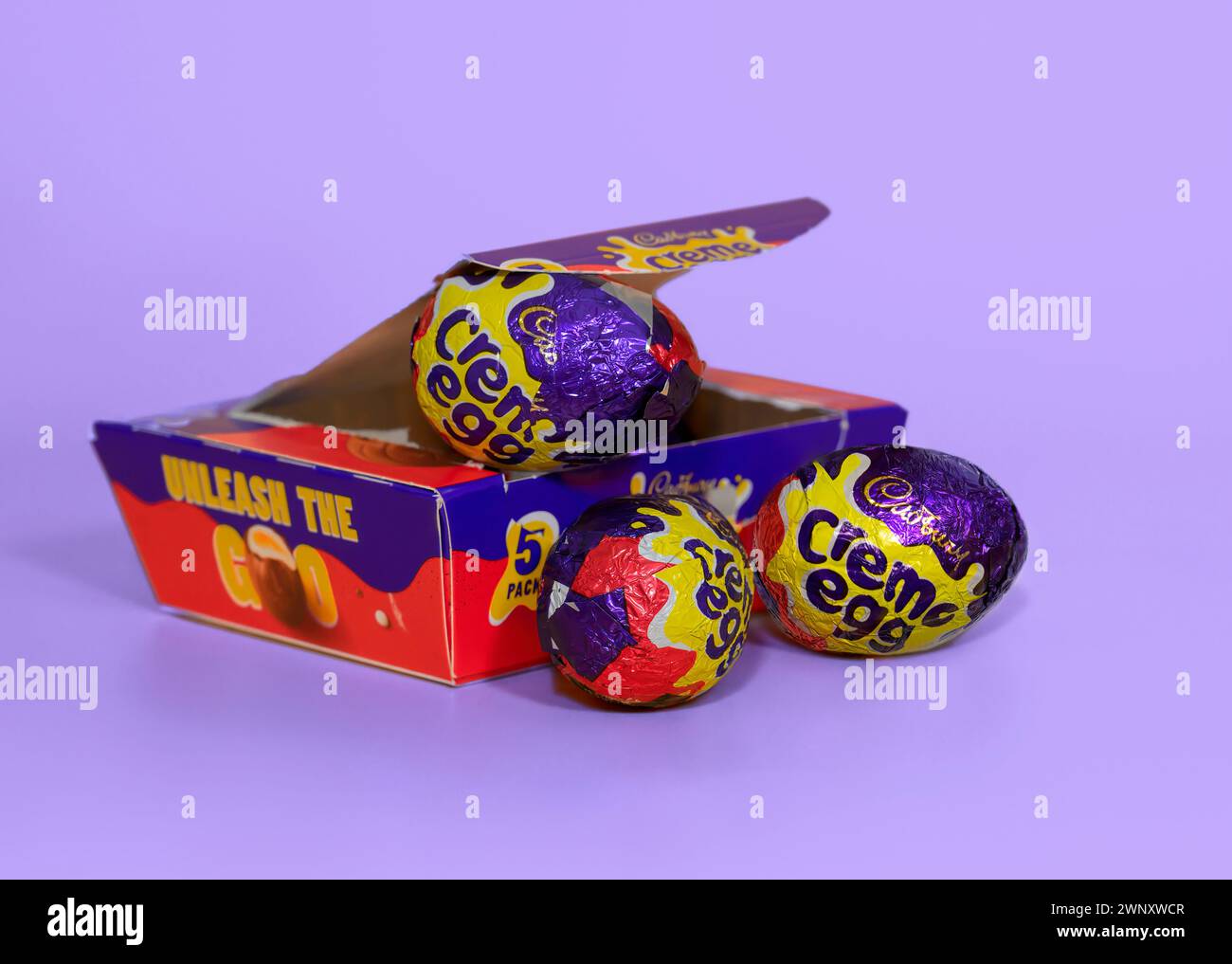 Boîte ouverte d'oeufs Cadbury Creme ouverts sur un fond violet clair avec deux oeufs crème devant Banque D'Images