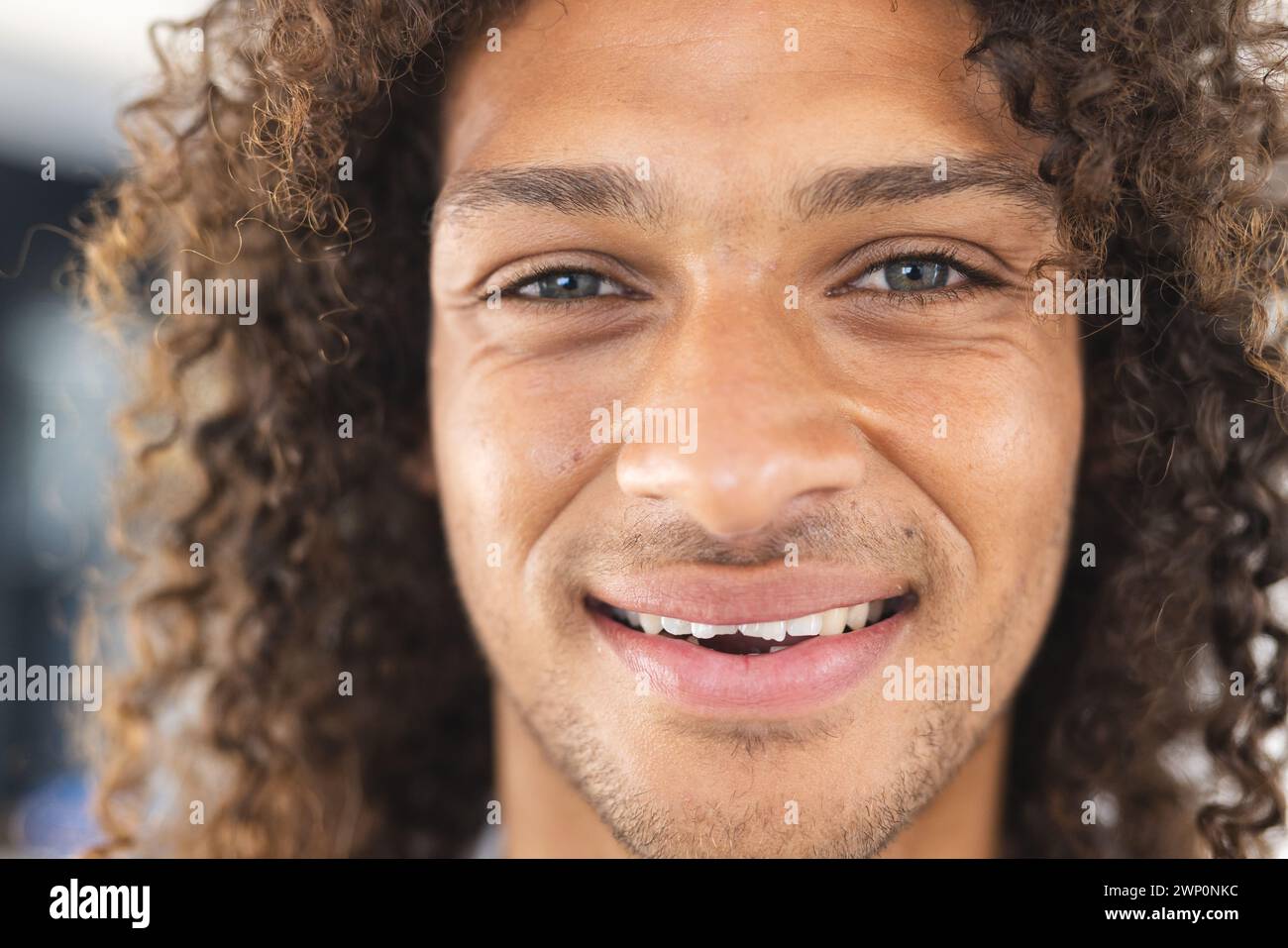 Un jeune homme biracial aux cheveux bouclés sourit chaleureusement à la caméra Banque D'Images