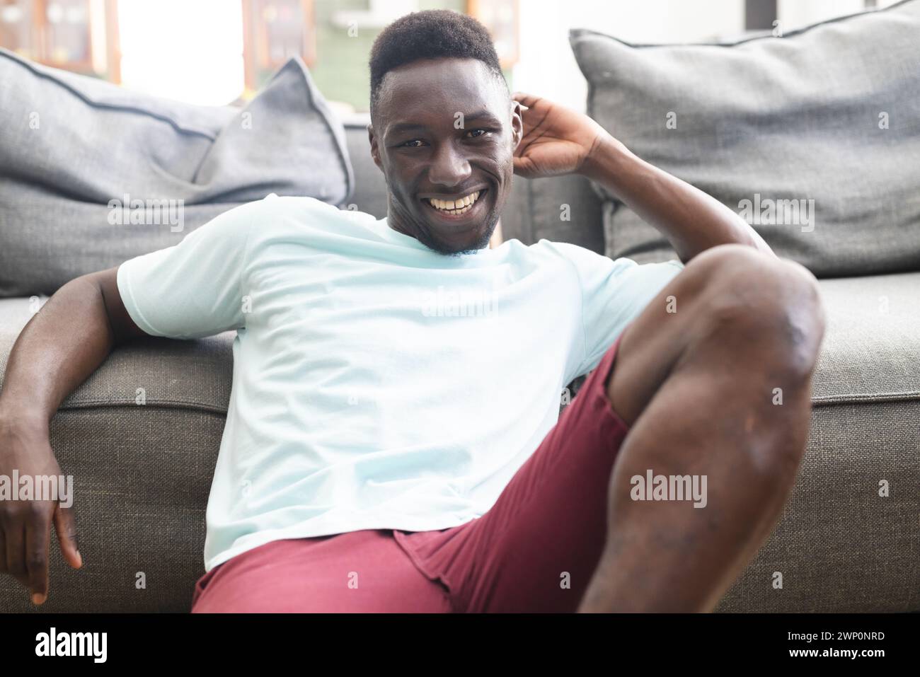 Jeune homme afro-américain se prélasse sur un canapé, souriant largement Banque D'Images