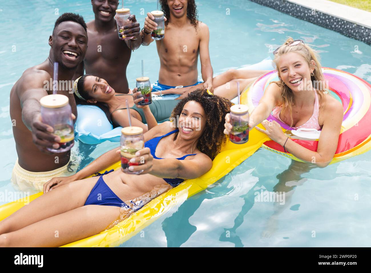 Groupe diversifié d'amis profitant d'une fête à la piscine, griller des boissons Banque D'Images
