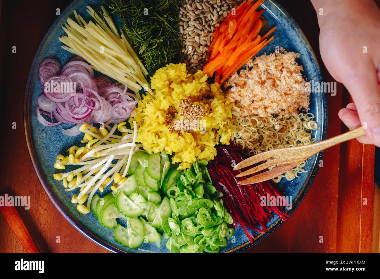 Une personne mange une salade avec une variété de légumes, y compris des carottes, du brocoli et des oignons. La salade est servie sur une assiette bleue et est placée dessus Banque D'Images