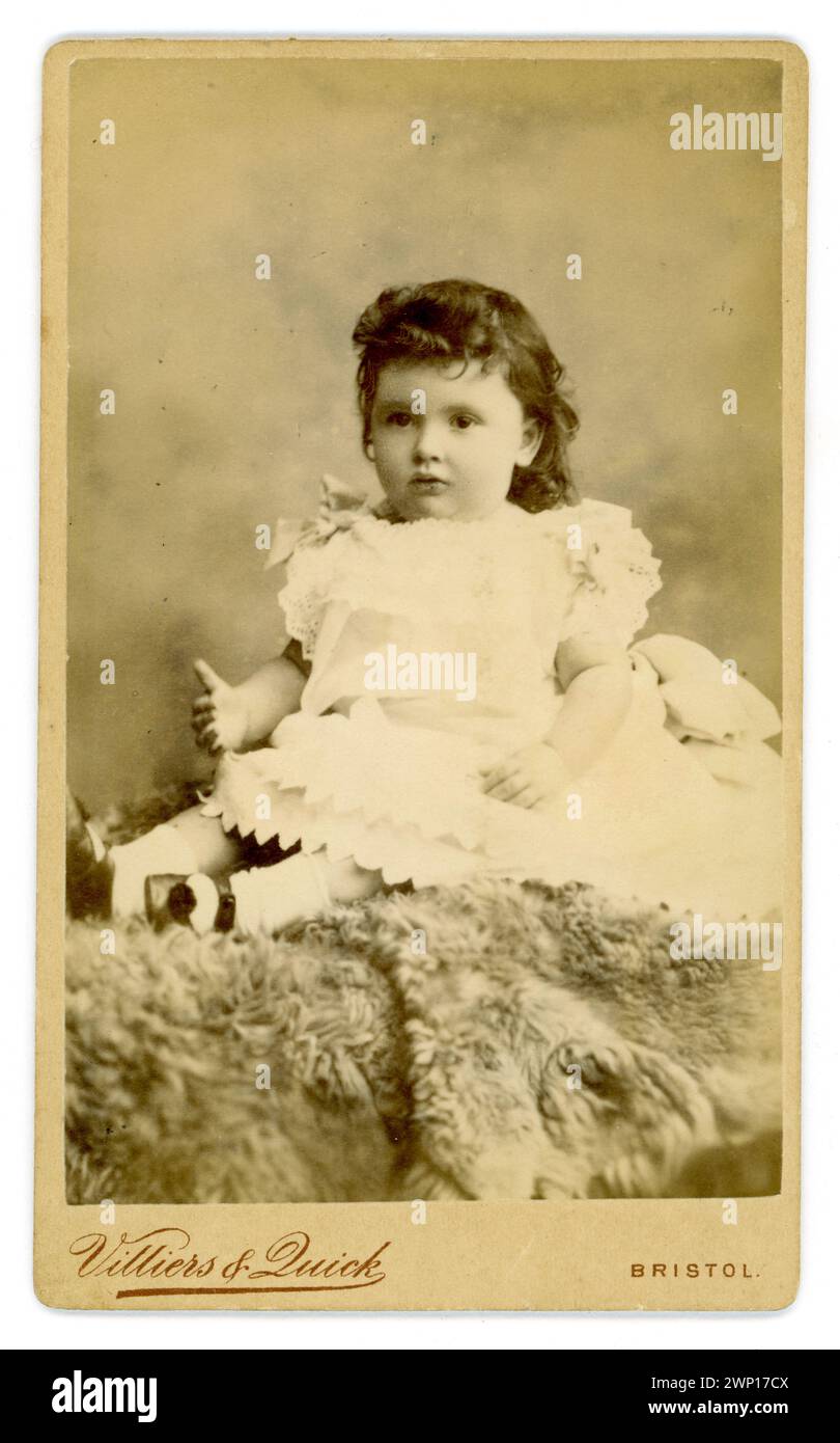 Original Charming Victorian carte de visite (carte de visite ou CDV) de jeune fille victorienne mignonne, enfant victorien, âgé d'environ 2 ans, avec des cheveux bouclés foncés, tapis de fourrure assis, Villiers & Quick, 42 Park Street, Bristol, Royaume-Uni vers la fin des années 1880 Banque D'Images