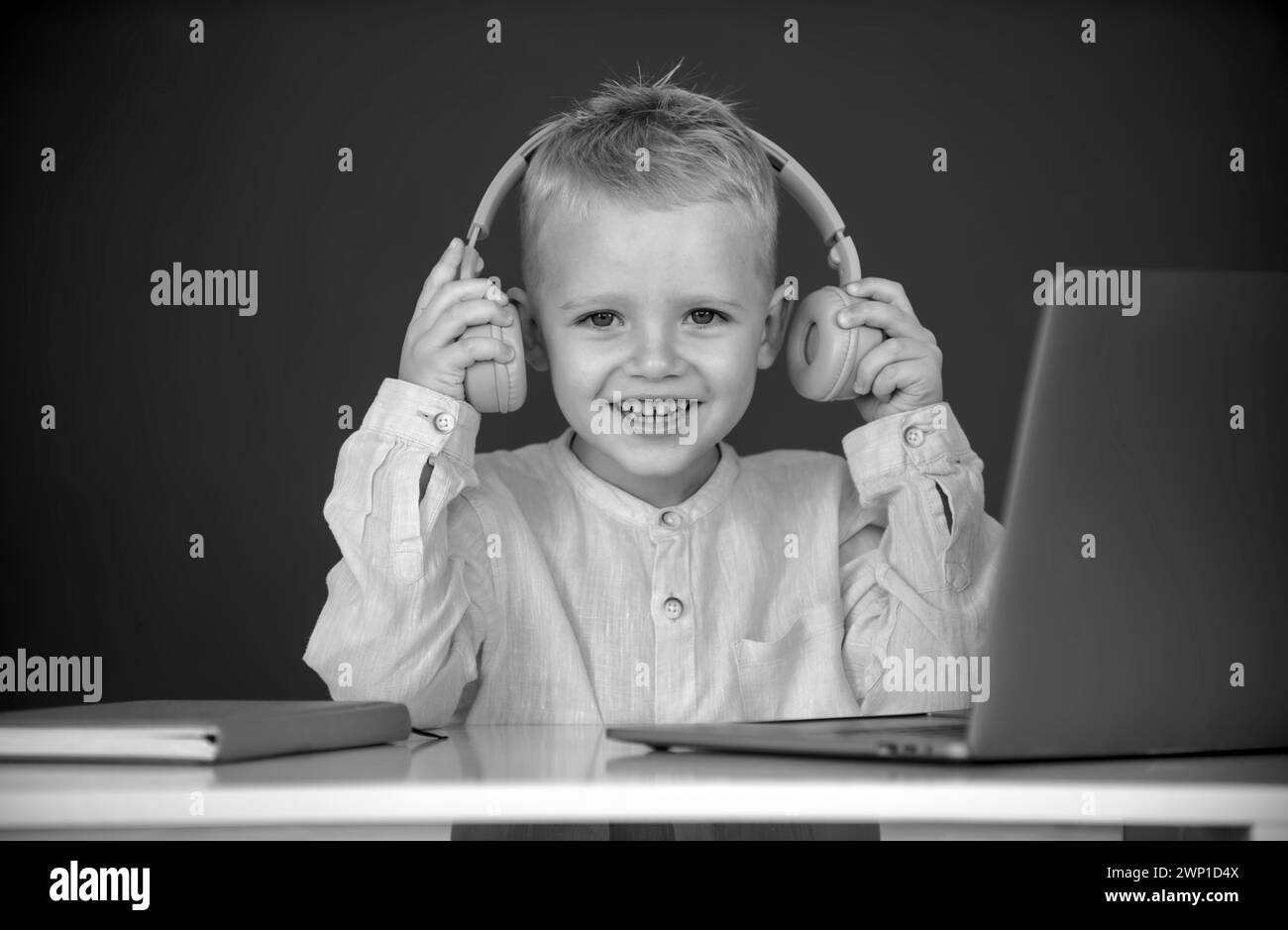 Smart boy dans un casque asseyez-vous au bureau, étudiez en ligne sur un ordinateur portable à l'école, klever Kid porter des écouteurs dans l'apprentissage d'ordinateur portable en utilisant des leçons d'Internet Banque D'Images