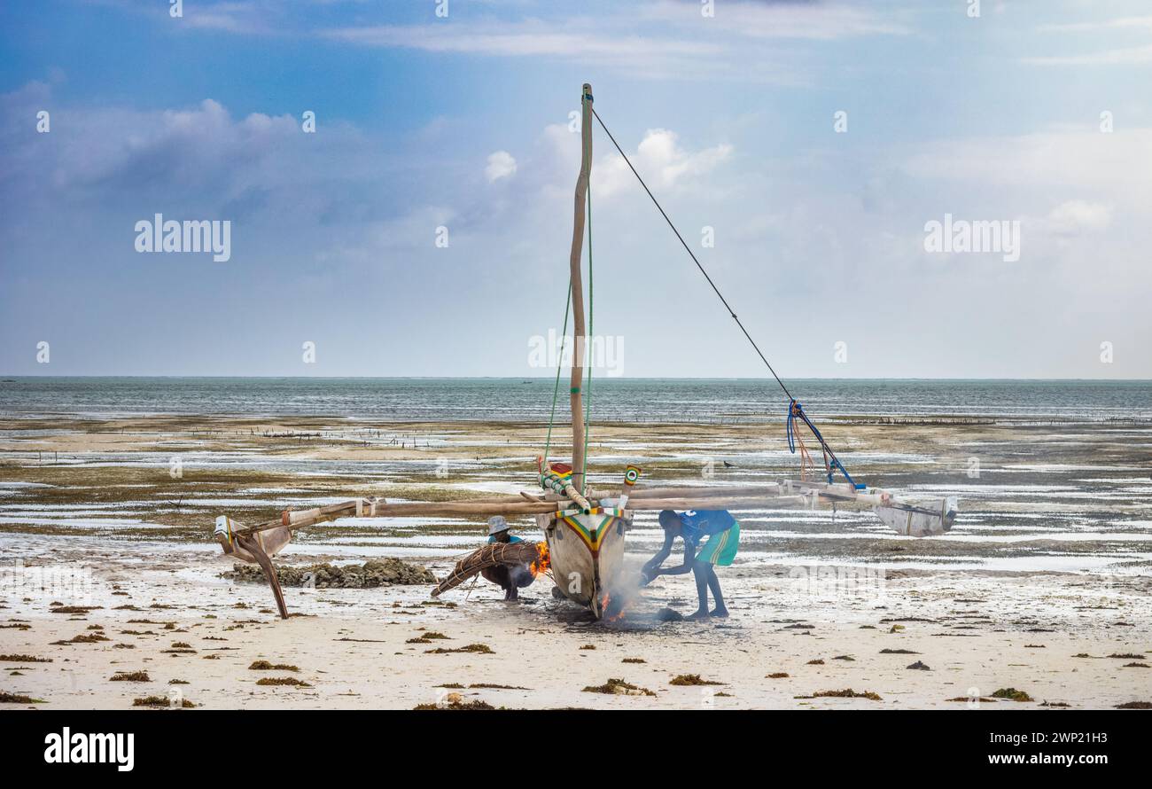 Les pêcheurs utilisent des frondes de palmier brûlantes pour ébavurer et imperméabiliser un bateau à boutre traditionnel en bois, Jambiani, Zanzibar, Tanzanie Banque D'Images