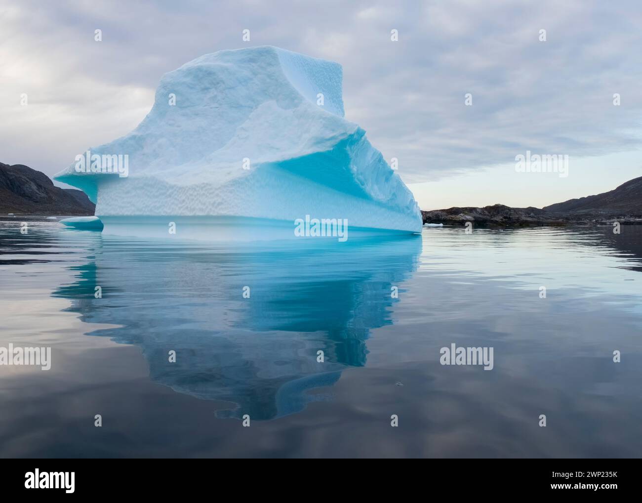 Grand iceberg de couleur bleue flotte sur l'eau calme dans la mer du fjord de Nanortalik au Groenland eau calme montrant la réflexion prise à la lumière de l'aube Banque D'Images
