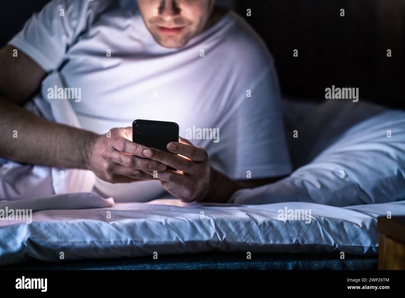 Homme au lit avec téléphone la nuit. Envoyer des SMS avec votre smartphone avant de dormir. Un gars tenant son téléphone portable à la main. Chambre à coucher sombre. Infidélité, tricherie. Banque D'Images