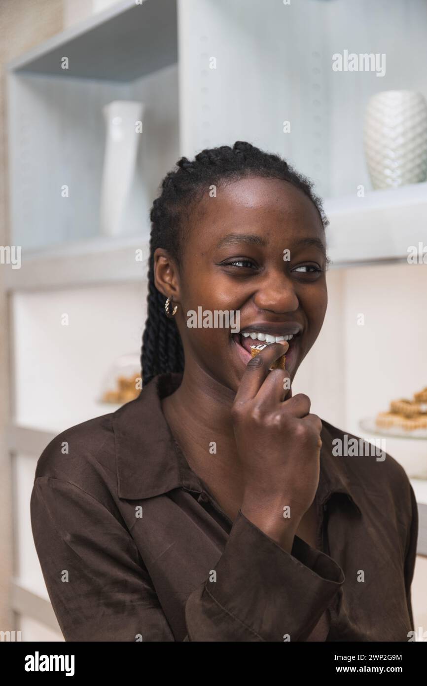Verticale photo une femme africaine apprécie un morceau de pâtes arabes, une sucrerie traditionnelle du moyen-Orient, dans une boulangerie spécialisée dans les desserts régionaux. Nourriture Banque D'Images