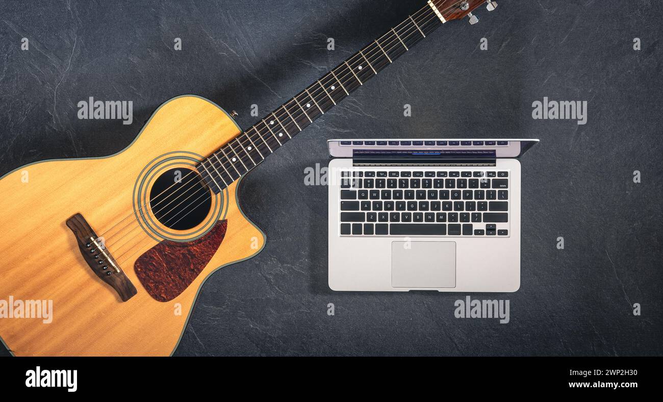 Guitare acoustique et ordinateur portable sur un fond noir texturé, vue de dessus. Banque D'Images
