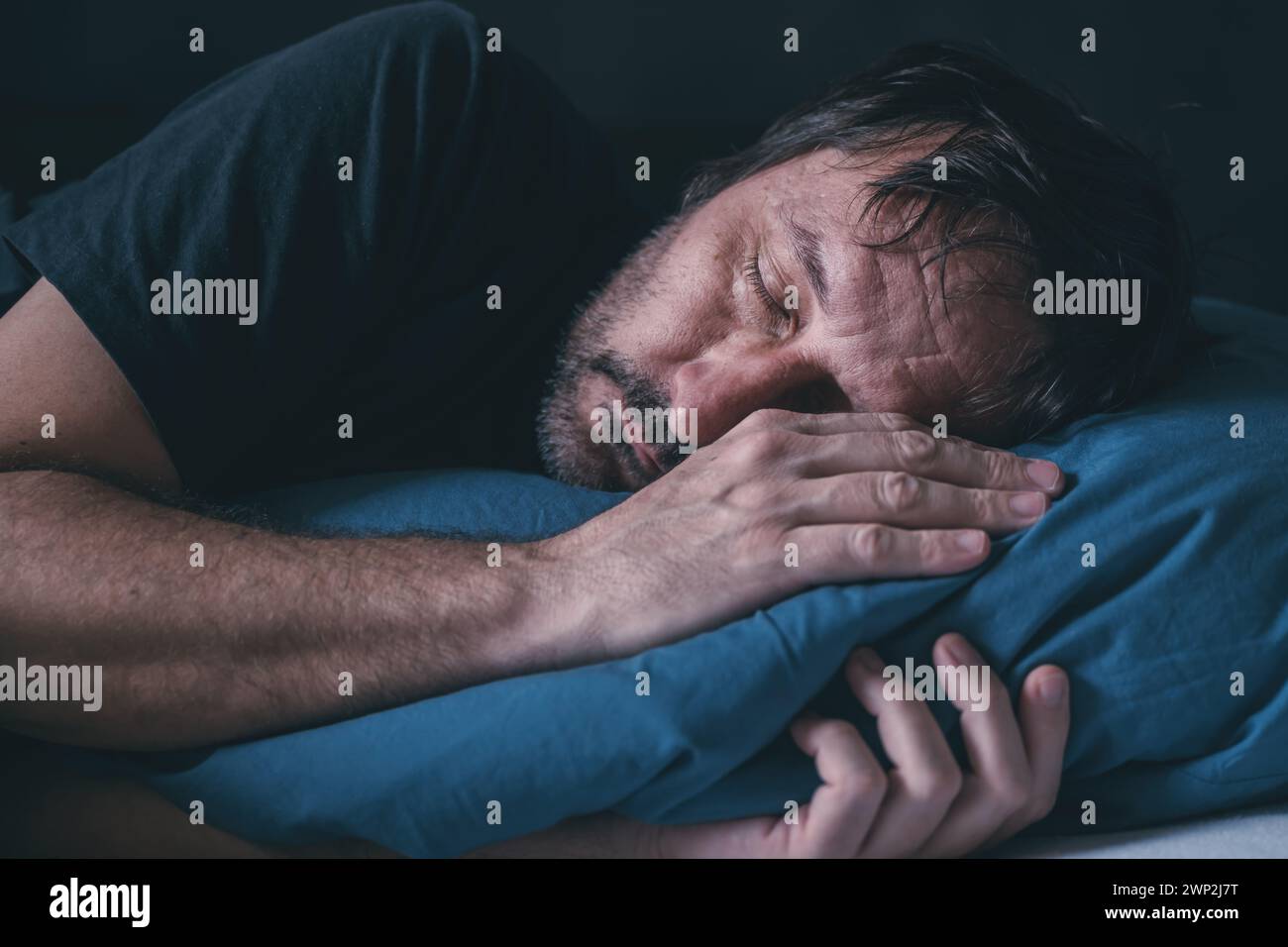Fatigué endormi mâle adulte dans un lit sur oreiller bleu, mise au point sélective Banque D'Images