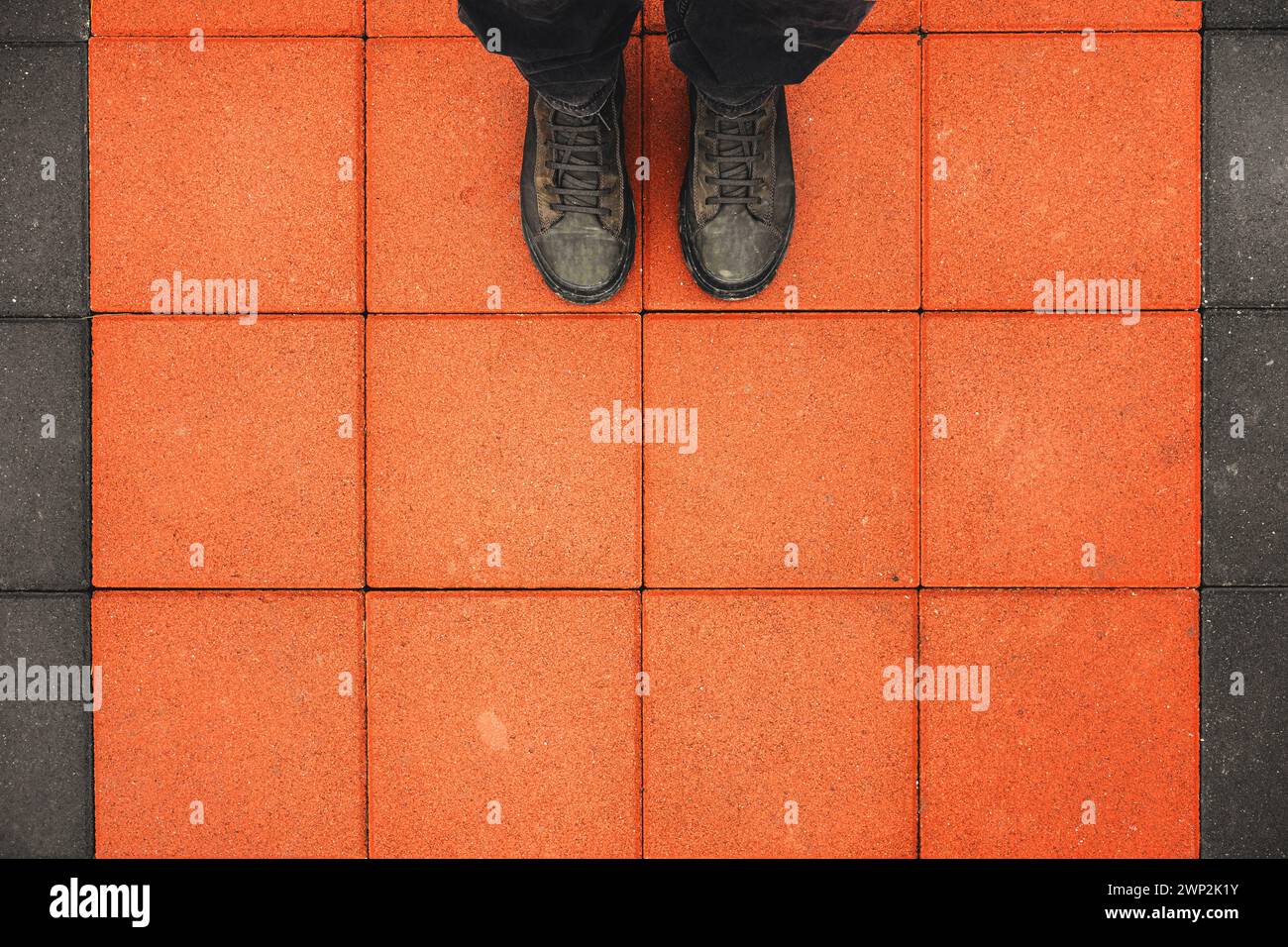 Homme debout sur les dalles carrées en béton, vue de dessus de bottes sales sur le trottoir orange avec espace de copie Banque D'Images