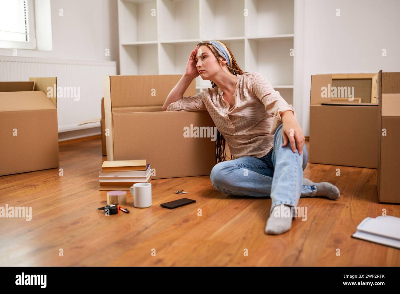 Femme de gingembre fatiguée avec des tresses assis sur le sol dans son nouvel appartement. Elle est épuisée de bouger. Banque D'Images
