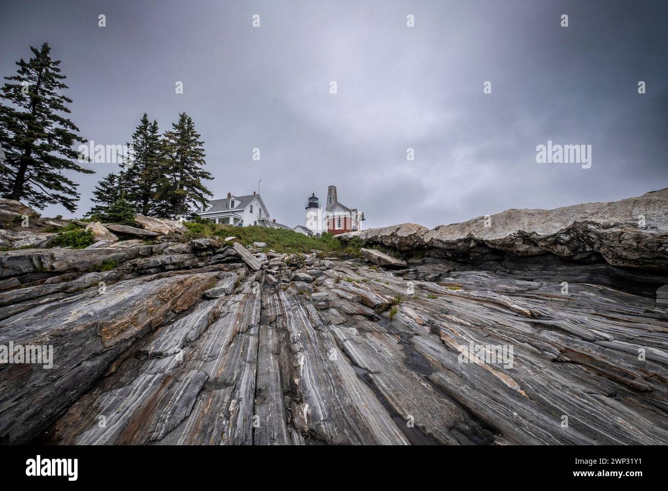 Le phare à Pemaquid Point, Maine avec ciel nuageux au-dessus et les corniches rocheuses massives à l'avant-plan. Banque D'Images