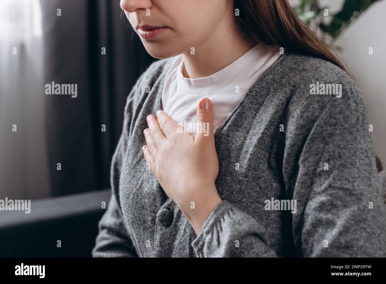 Gros plan de la jeune femme bouleversée ressentant une forte douleur dans la poitrine, se tortillant dans la douleur, assise seule sur le canapé à la maison. Menace de crise cardiaque. Les maladies ont fréquenté Banque D'Images
