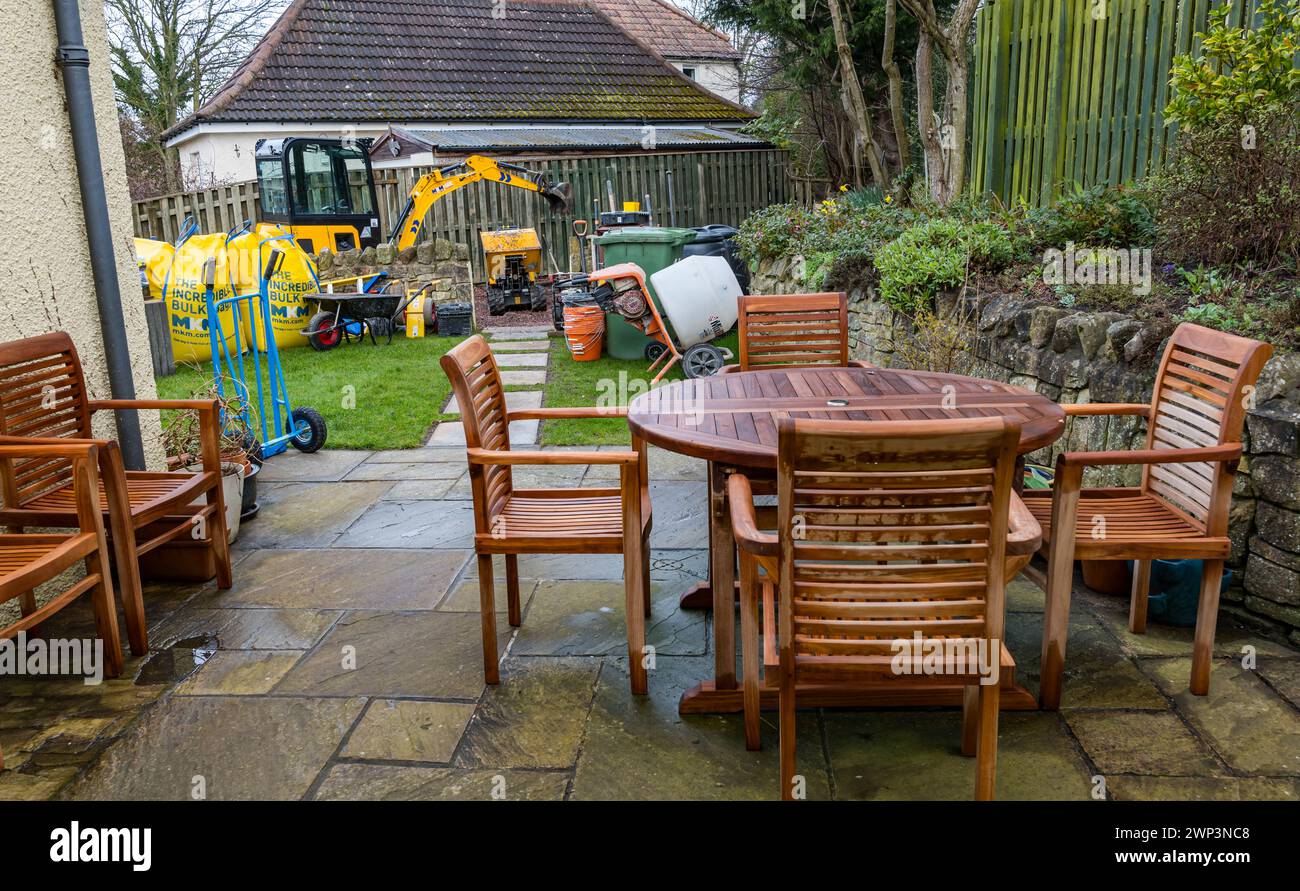 Travaux de construction avec une petite excavatrice et des matériaux de construction dans l'allée avec meubles de jardin patio, Écosse, Royaume-Uni Banque D'Images