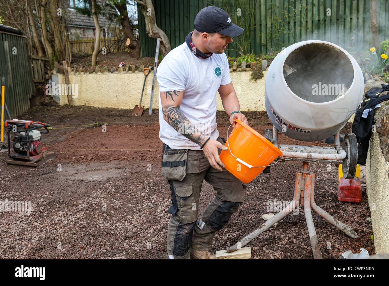 Ouvrier remplissant mélangeur de ciment pour des travaux de construction dans une allée pour construire une salle de jardin, Écosse, Royaume-Uni Banque D'Images