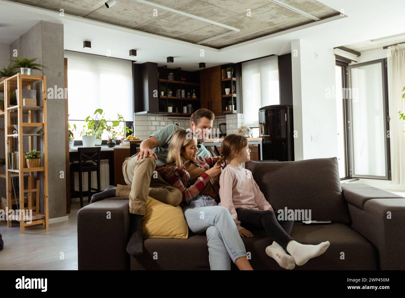 La famille profite d'un moment de détente ensemble sur le canapé, avec des interactions ludiques et des sourires chaleureux Banque D'Images