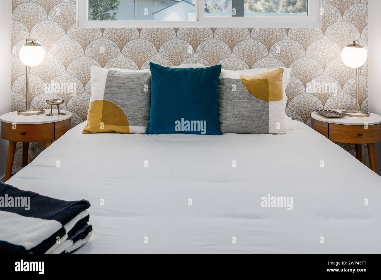 Chambre moderne avec lit confortable, oreillers, tables de nuit et papier peint en mosaïque Banque D'Images