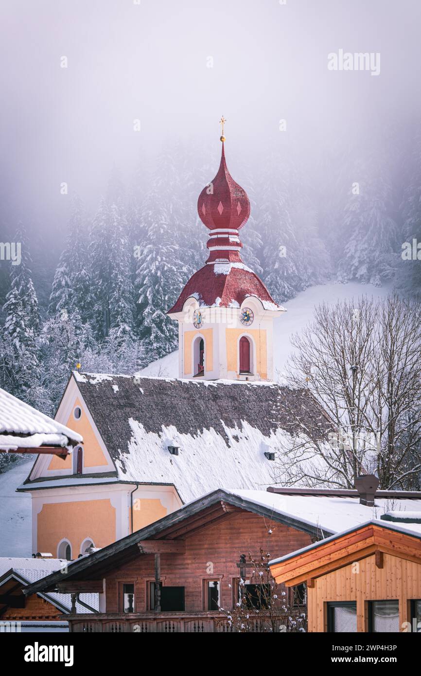 Un village en hiver avec une église à dôme rouge devant une forêt enneigée, le Mountain Doctor, Going, Autriche Banque D'Images