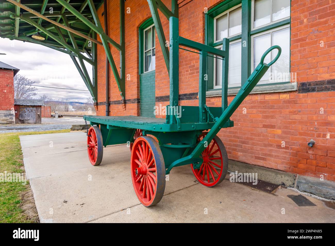 Chariot à bagages en bois vert vintage avec quatre roues de wagon le long d'un bâtiment en briques. Banque D'Images