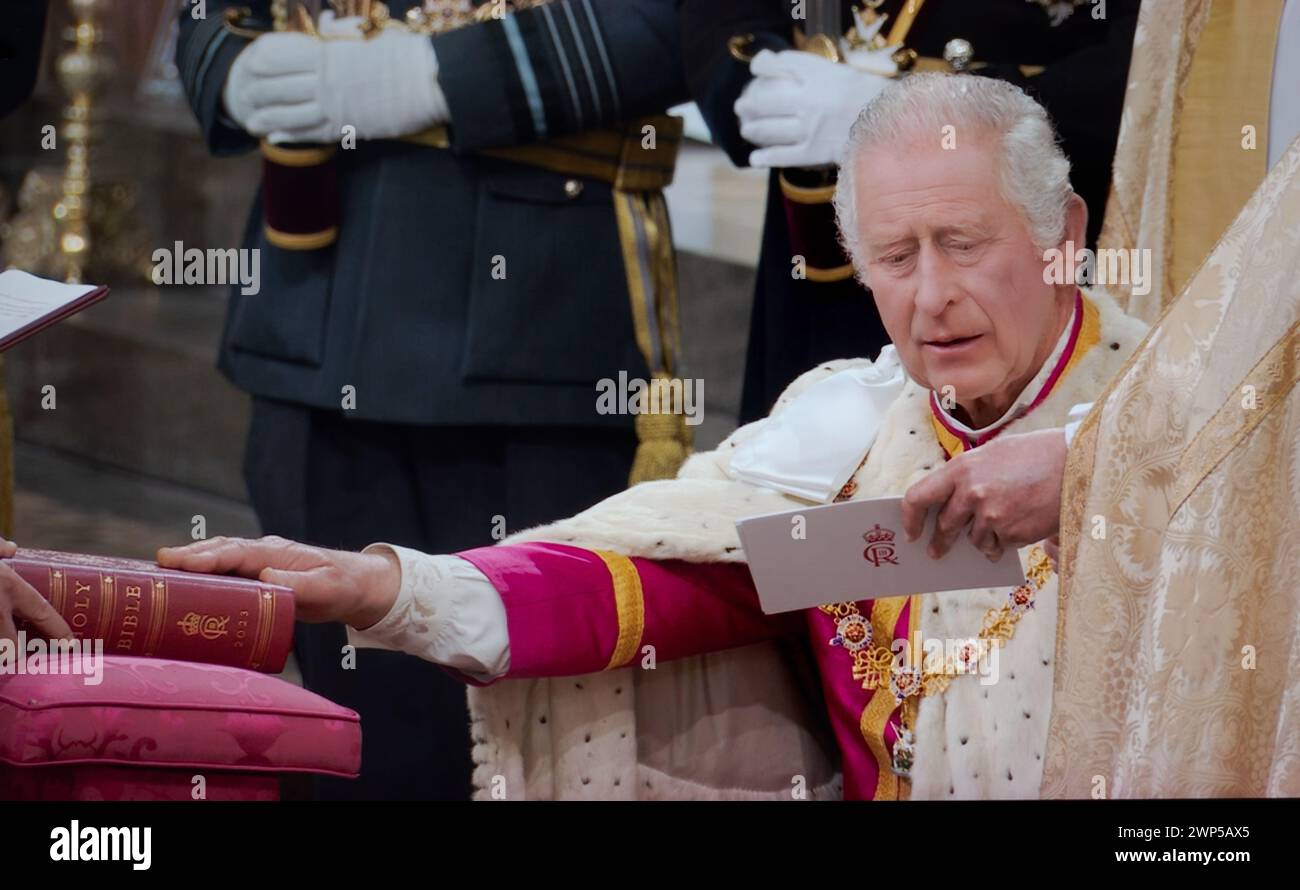 Le roi Charles III couronnement, assis dans des robes de cérémonie, prête le serment solennel couronnement touchant la Sainte Bible gravée avec ses souverains Cypher et date, lors de la cérémonie de service du couronnement à l'abbaye de Westminster Westminster Londres Royaume-Uni le 6 mai 2023 Banque D'Images