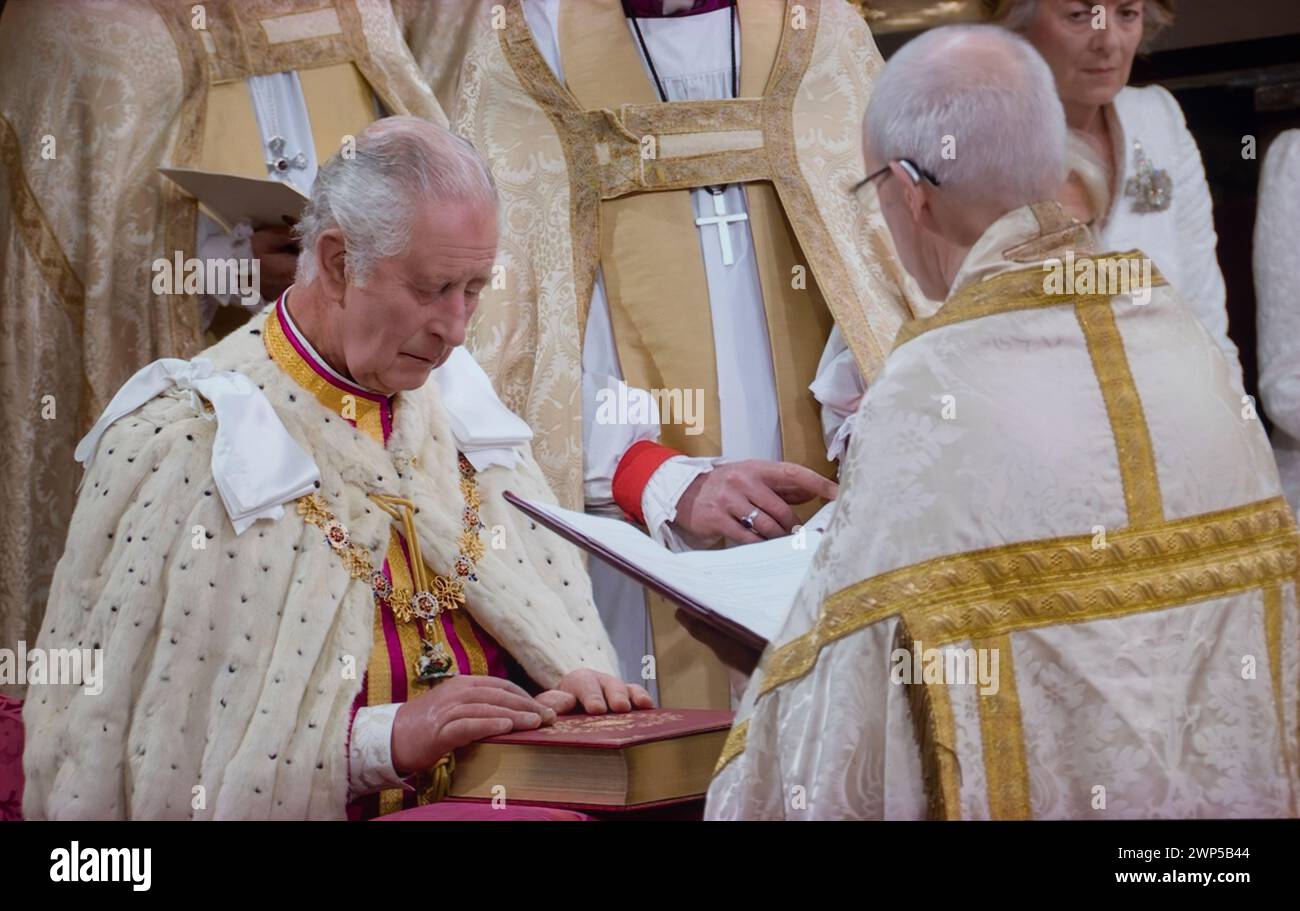Le roi Charles III couronnement, assis dans des robes de cérémonie, prête serment solennel couronnement, avec l'archevêque Justin Welby, touchant la Sainte Bible gravée avec ses souverains Cypher et date, lors de la cérémonie de couronnement à l'abbaye de Westminster Westminster Londres Royaume-Uni le 6 mai 2023 Banque D'Images