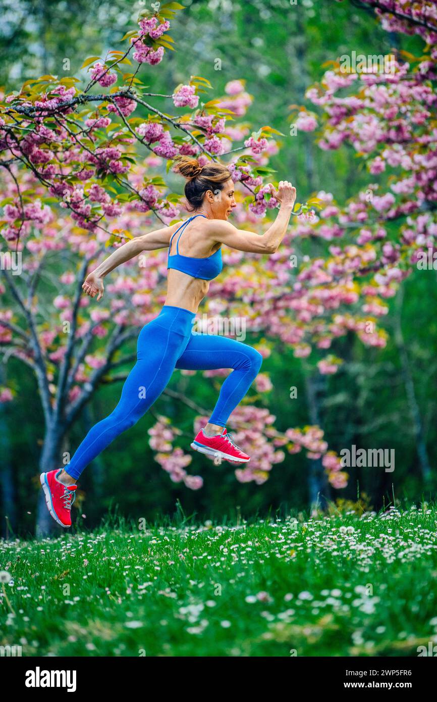 Athlète féminine s'entraînant portant des vêtements de sport parmi les cerisiers Banque D'Images