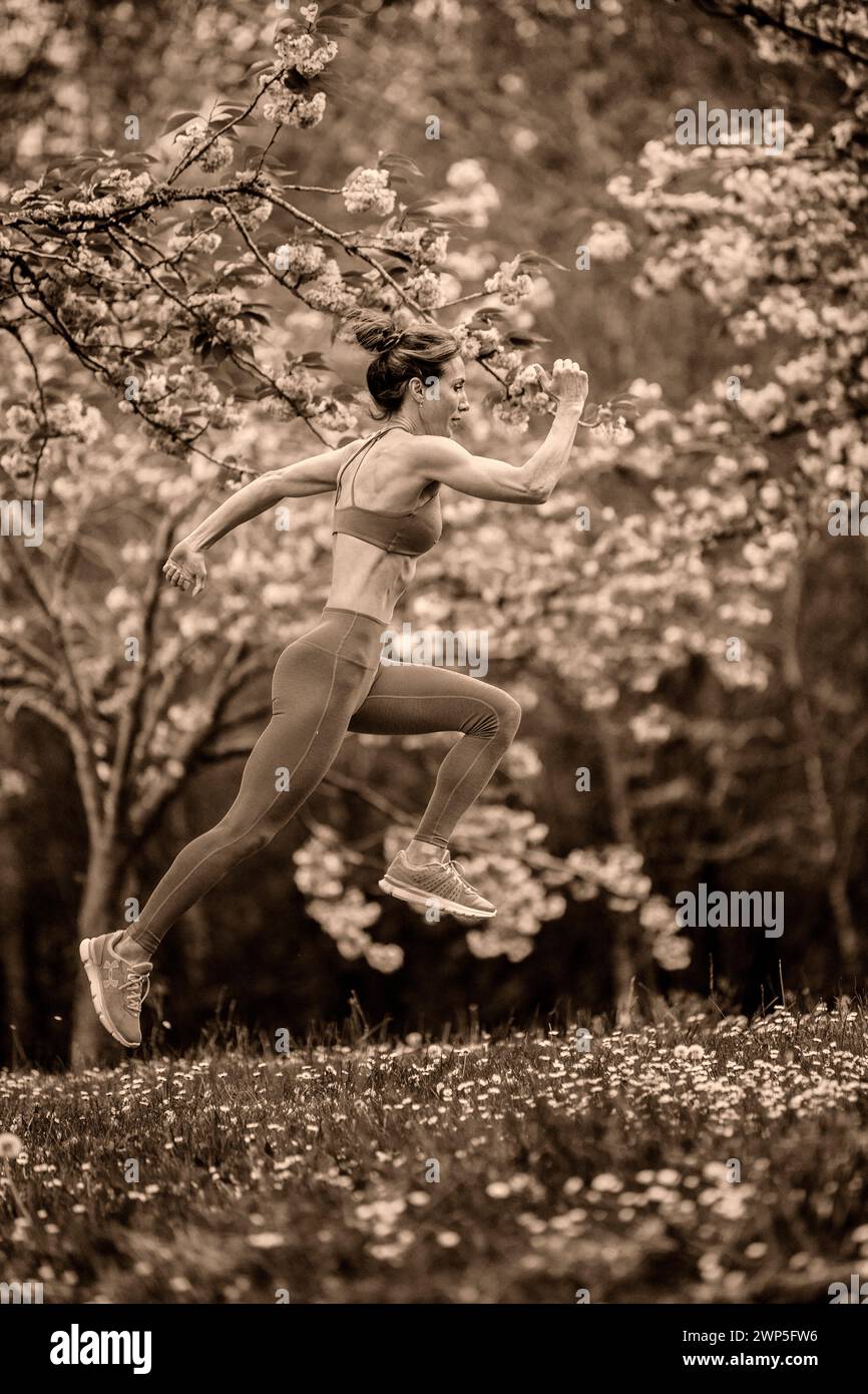 Athlète féminine s'entraînant portant des vêtements de sport parmi les cerisiers Banque D'Images