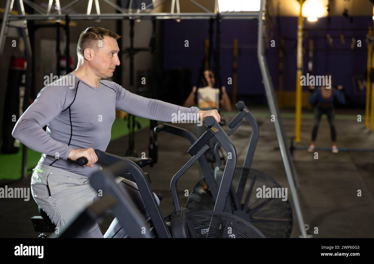 Homme actif faisant de l'entraînement cardio sur vélo stationnaire cross training dans le gymnase Banque D'Images