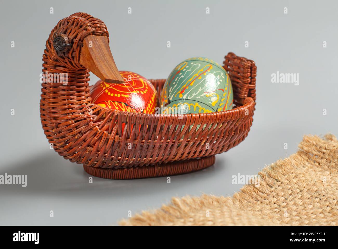 Oeufs de Pâques colorés dans le panier en osier avec un sac de sac sur le fond gris. Banque D'Images