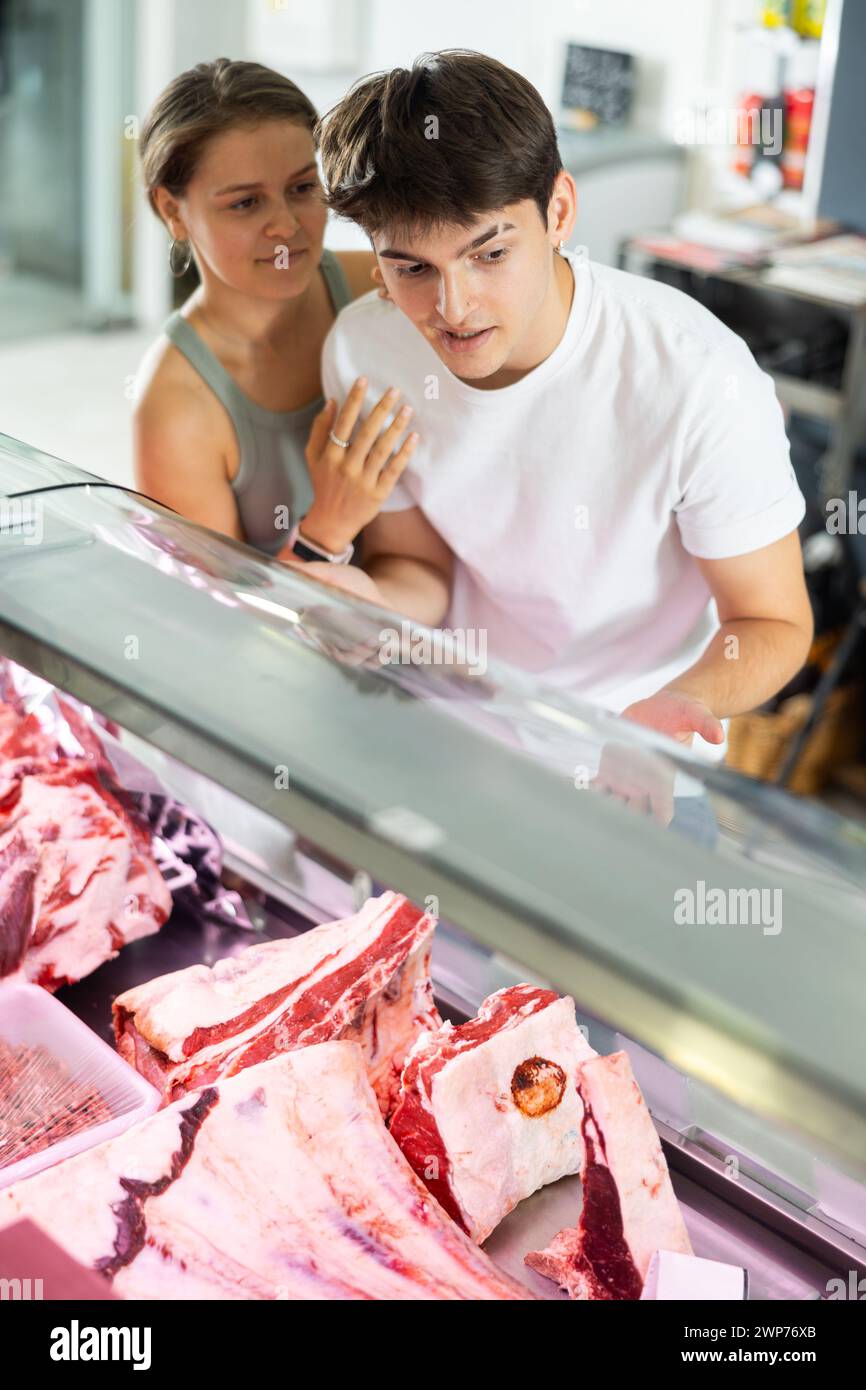 Conjoint près de la fenêtre de boucherie inspecte les marchandises et choisit un morceau de boeuf pour la cuisson du steak d'oeil de côte Banque D'Images