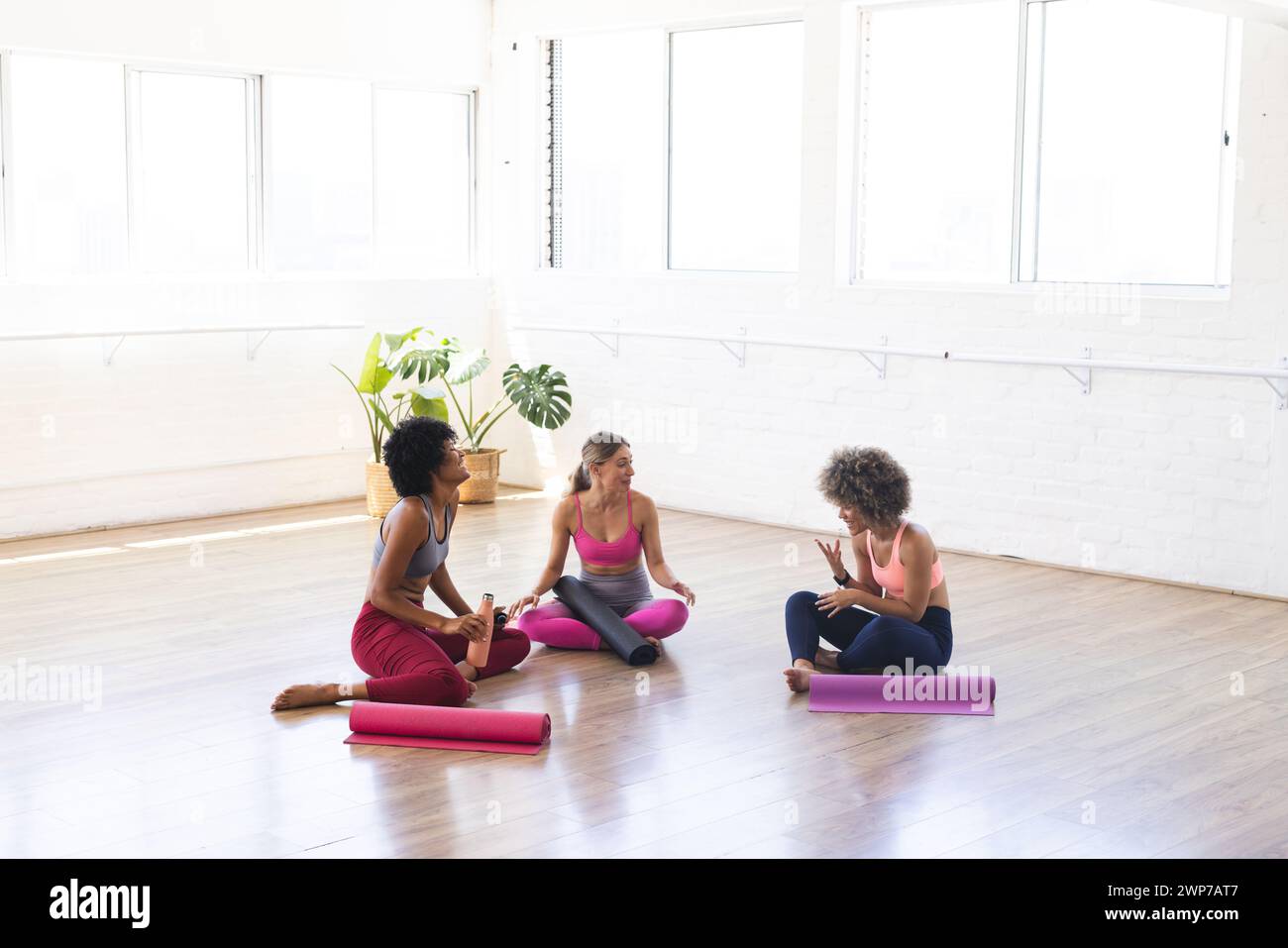 Jeune femme caucasienne discute avec des femmes biraciales dans un studio de yoga lumineux avec espace de copie Banque D'Images