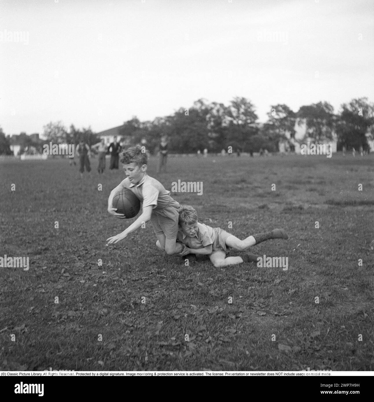 Rugby 1940. Les jeunes joueurs de rugby pratiquent ensemble. le garçon qui court avec le ballon de rugby est vu être attaqué par un autre garçon. Le ballon de rugby a une forme ovale, quatre panneaux et un poids d'environ 400 grammes. 1942. Kristoffersson ref A58-6 Banque D'Images